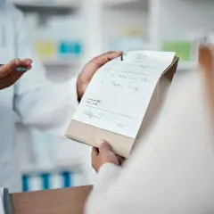 Farmaceuta w białym fartuchu podaje pacjentowi receptę i torebkę z lekami.