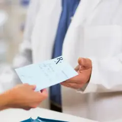 Farmaceuta w białym fartuchu podaje receptę. Dowiedz się, jak odzyskać kod recepty, aby zrealizować leki.