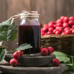 Butelka z nalewką z glogu na spirytusie, obok gałązka z owocami i kosz pełen głogu.