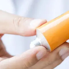 Dłonie wyciskają popularną maść z antybiotykiem z pomarańczowej tubki.