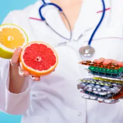 Lekarz trzyma połówki grejpfruta i pomelo, ostrzegając przed popijaniem leków sokiem grejpfrutowym.