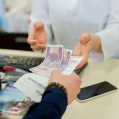Dłoń podaje farmaceucie polskie banknoty i receptę.