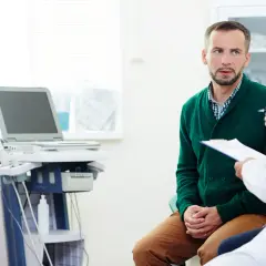 Mężczyzna w zielonym swetrze rozmawia z lekarzem w gabinecie urologicznym, obok aparat USG.