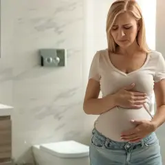 Kobieta w ciąży trzyma się za brzuch, zmartwiona. Czy to wzdęcia, czy skurcze w ciąży?
