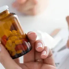 Kobieta trzyma buteleczkę z tabletkami, zastanawiając się nad pominięciem dawki leku Euthyrox. Obok ktoś notuje.