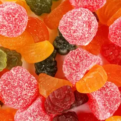 Kolorowe żelki, w tym czerwone kulki w cukrze, pomarańczowe kawałki i zielone listki. Czy żelki są zdrowe? Raczej nie, to słodka przekąska.