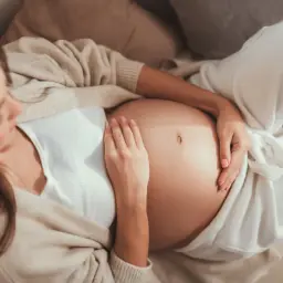 Kobieta w ciąży delikatnie dotyka brzucha. Czas oczekiwania na dziecko, czyli ile trwa ciąża, jest pełen emocji.