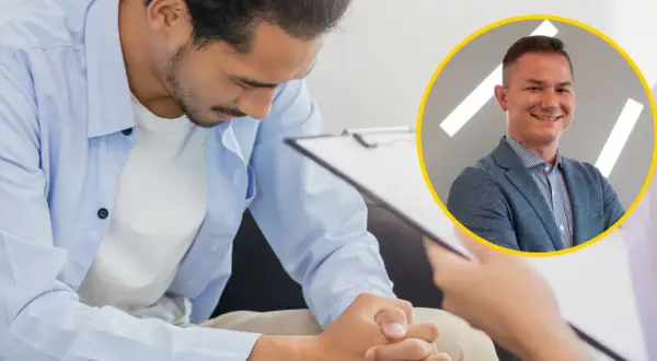 Mężczyzna w niebieskiej koszuli pochyla się nad dokumentami, obok uśmiechnięty urolog. Tak wygląda badanie prostaty u urologa.