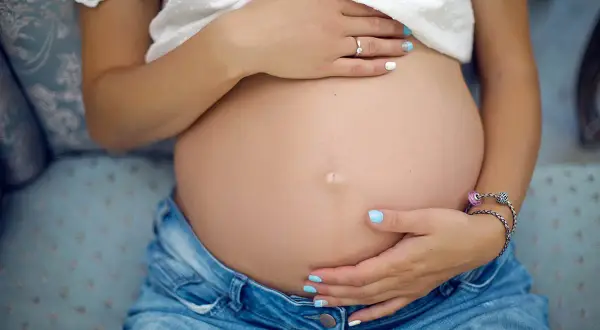 Brzuszek w jeansach, dłonie delikatnie go obejmują. To piękny moment, kiedy zaczyna się trzeci trymestr ciąży.