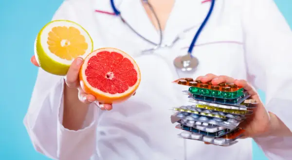 Lekarz trzyma połówki grejpfruta i pomelo, ostrzegając przed popijaniem leków sokiem grejpfrutowym.