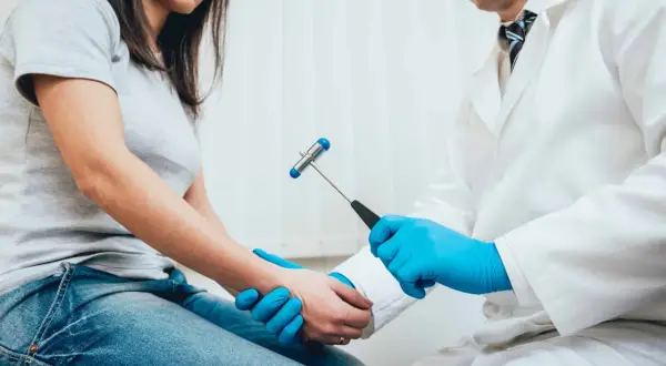 Neurolog w białym kitlu bada pacjentkę młoteczkiem neurologicznym. To dowód, że szuka się najlepszego neurologa w Polsce.