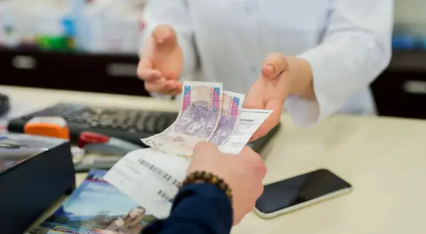 Dłoń podaje farmaceucie polskie banknoty i receptę.