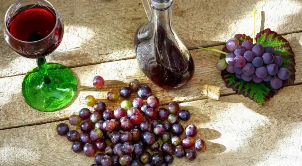 Nalewka z winogron na spirytusie w karafce, kieliszek z winem, winogrona i korek na drewnianym stole.