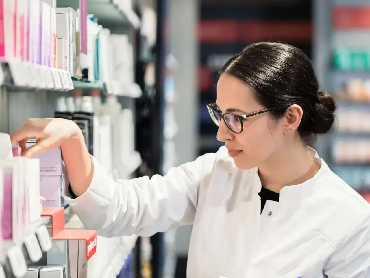 Farmaceutka w okularach wybiera produkt z półki. Dowiaduje się, co to jest ryczałt na recepcie, szukając informacji.